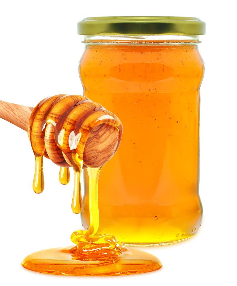 白色背景下装在玻璃瓶中的金黄色的美味的蜂蜜