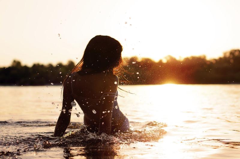 日落时在海洋中的性感女人背影