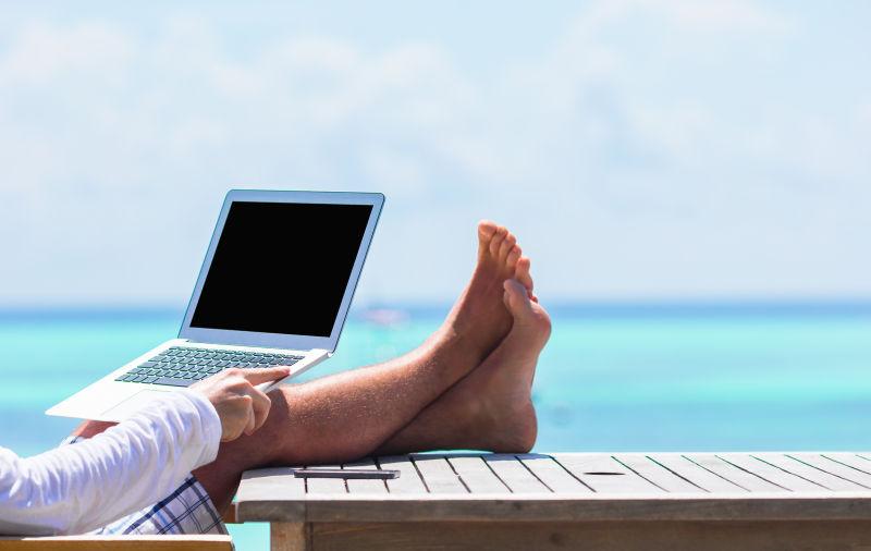 阳光下双脚搭在木桌上的男人拿着笔记本电脑