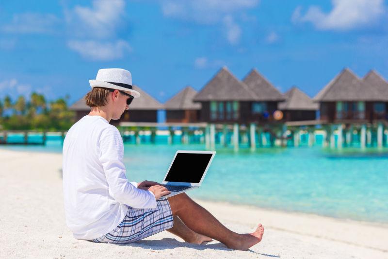 坐在沙滩上使用笔记本电脑的年轻男人