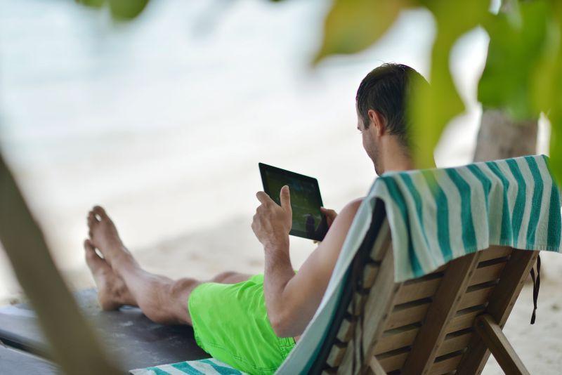 靠在沙滩椅上使用平板电脑的年轻男人