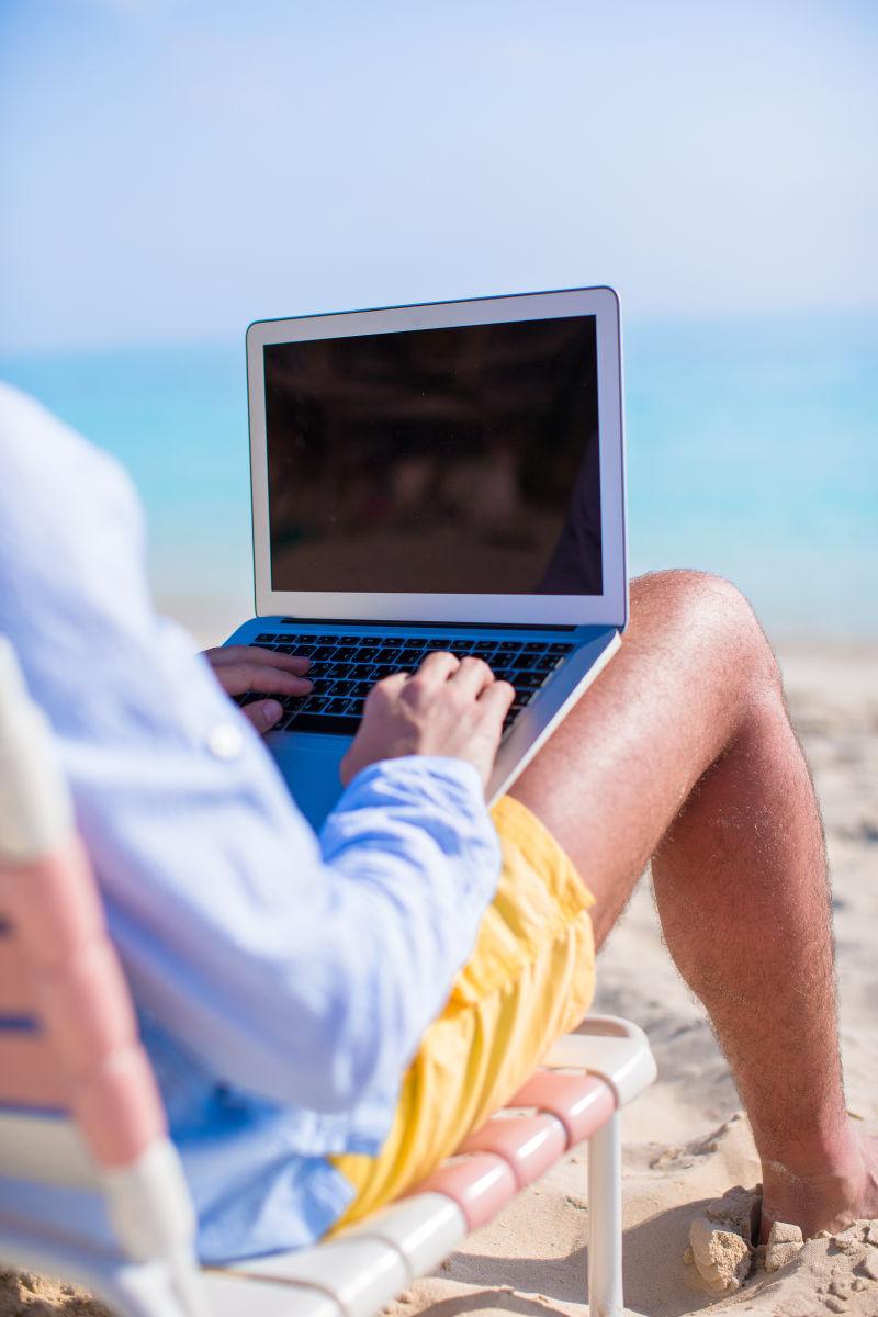 坐在沙滩椅上使用笔记本电脑的年轻人