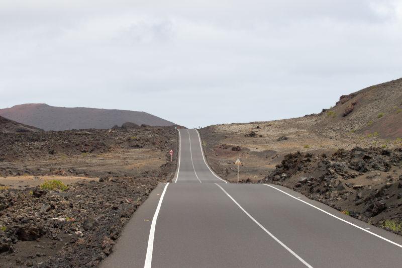 有云的天空下的黄色山坡上的公路