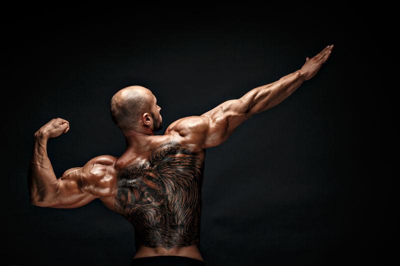 背部纹身的肌肉男子在黑色背景上