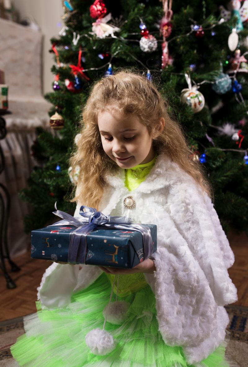 圣诞树前拿着礼盒的金发小女孩