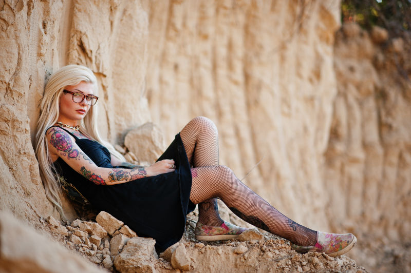 年轻的纹身金发女孩靠坐在岩石上
