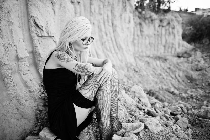 纹身金发女孩坐在岩石上