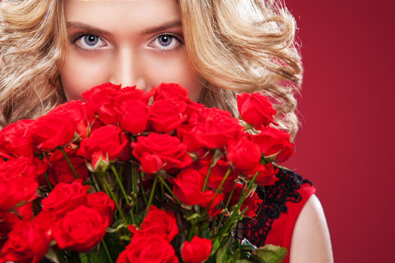 美丽的金发女人捧着一束红玫瑰