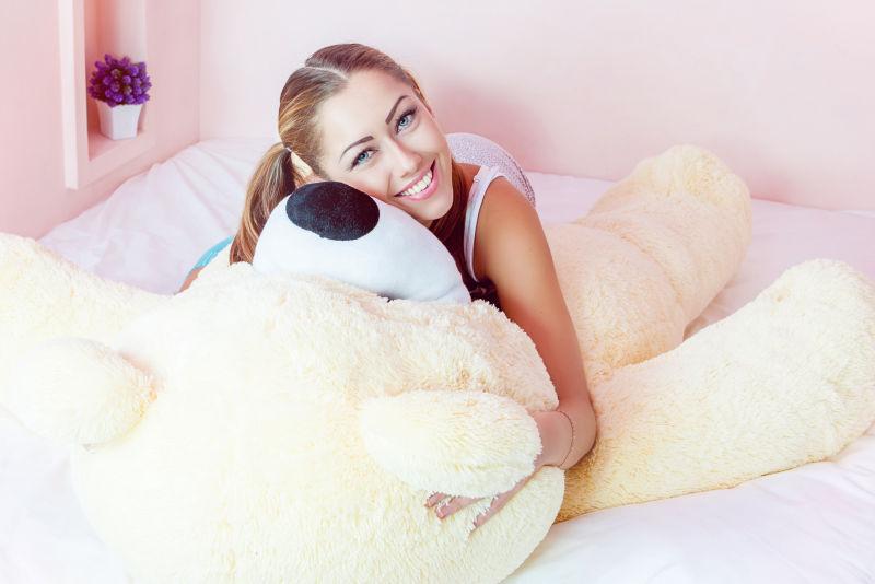 在床上抱着大玩具熊的微笑女孩