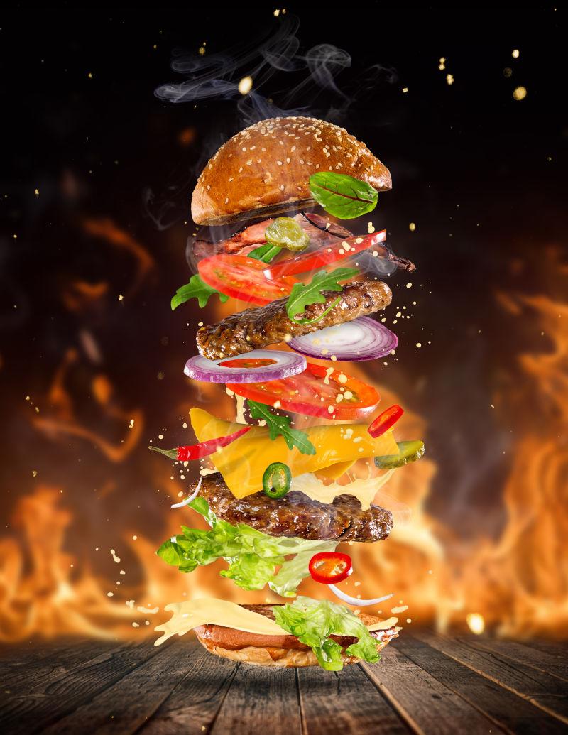 火焰背景中木桌面上飞起来的配料新鲜的巨大汉堡