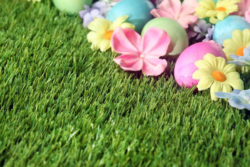 绿色草地上整齐摆放在一边的复活节彩蛋和花朵