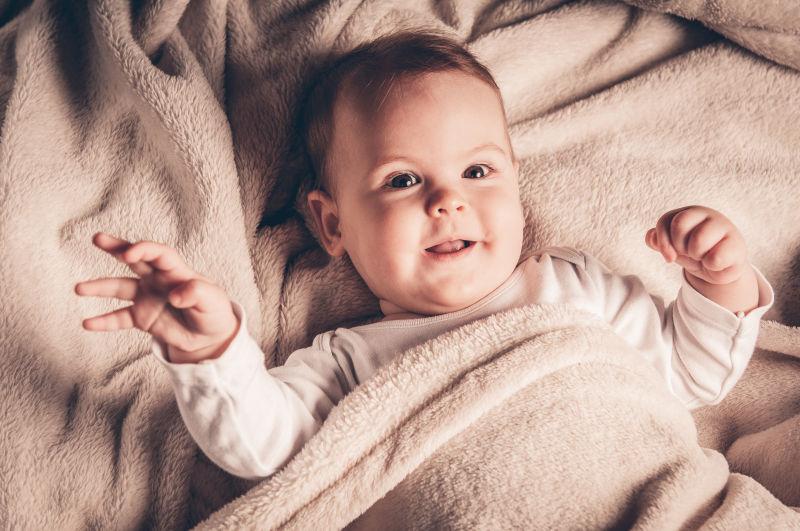 躺在灰色的毛毯上微笑的小女婴