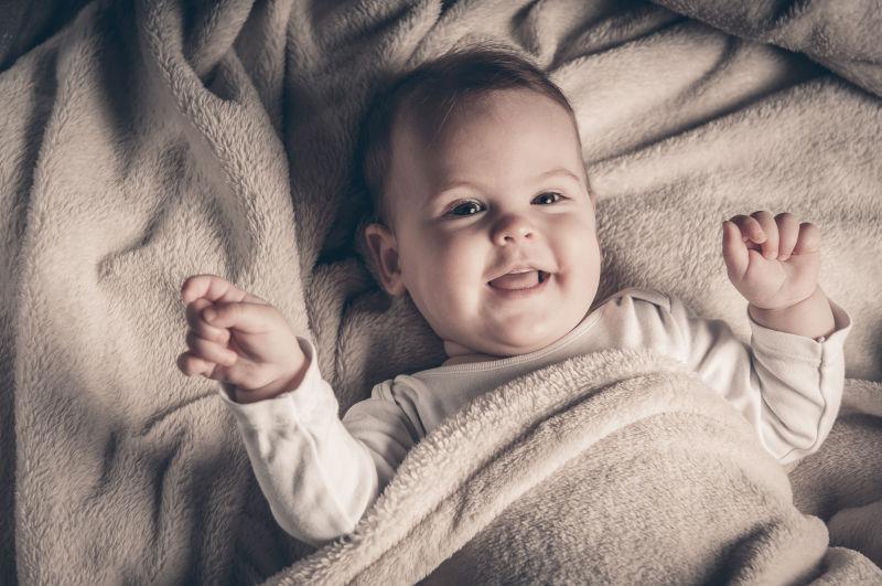躺在床上盖着毛毯的微笑的小婴儿