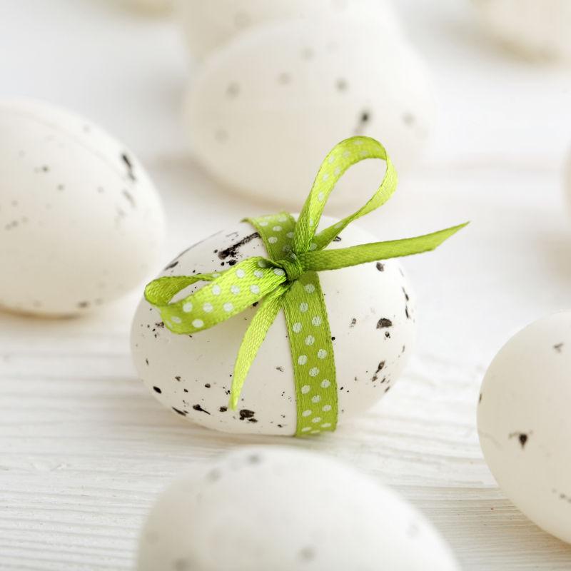 白色桌上的带有绿色蝴蝶结的复活节彩蛋