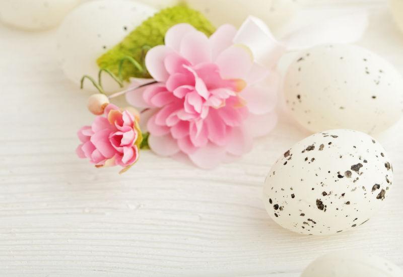 木纹理桌上的白色的复活节彩蛋和粉色花朵