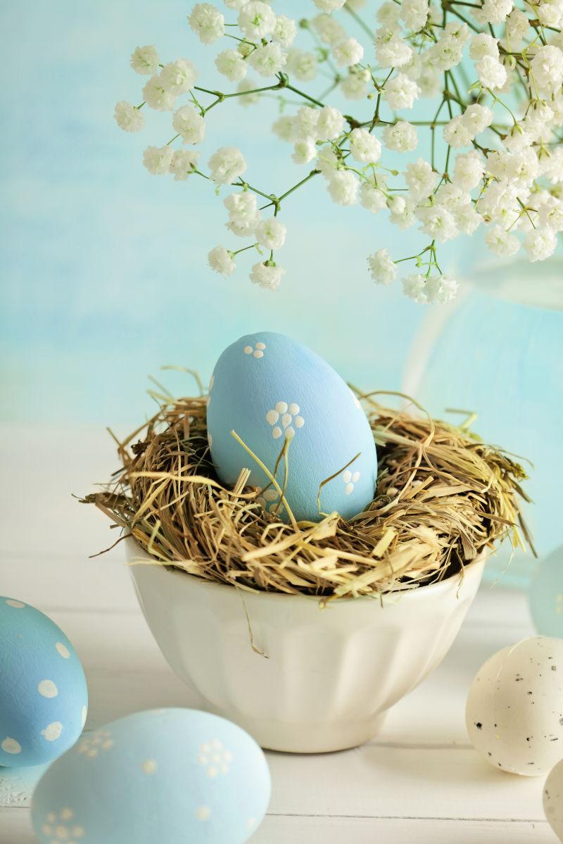 白色桌上白色满天星花朵背景下的安在碗里的鸟窝里的复活节彩蛋
