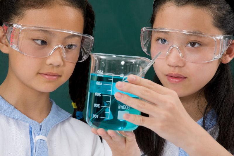 带着专业的眼镜观察烧杯内的化学反应的女学生