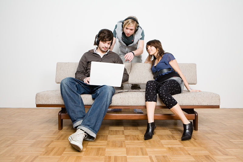 坐在沙发上看笔记本电脑的三个年轻人