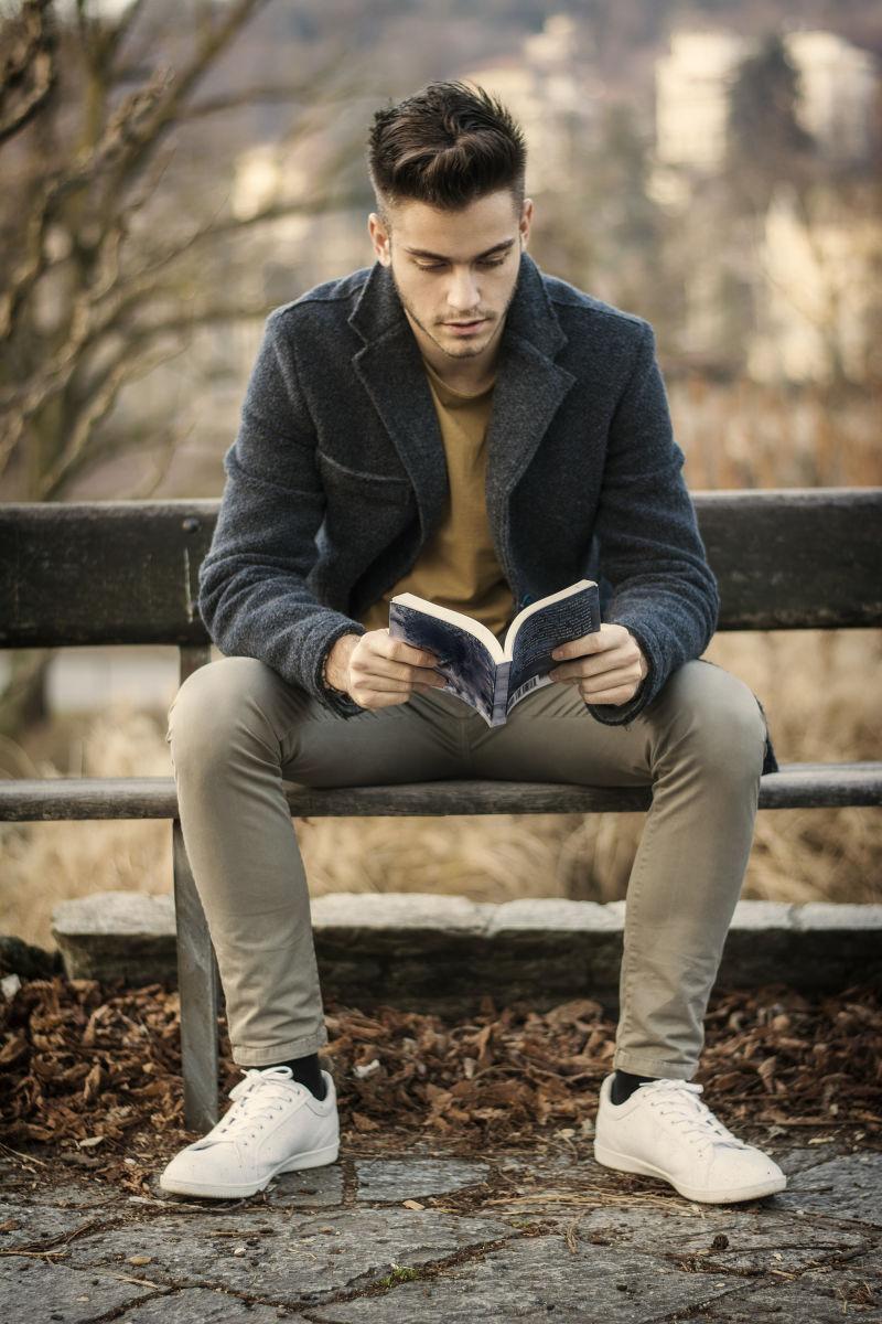时尚英俊的帅哥在公园里坐在长凳上看书