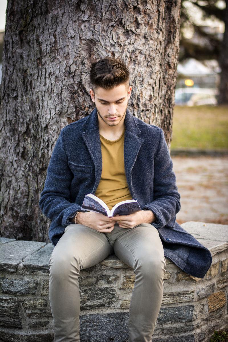 英俊的年轻人在公园里坐在长凳上看书