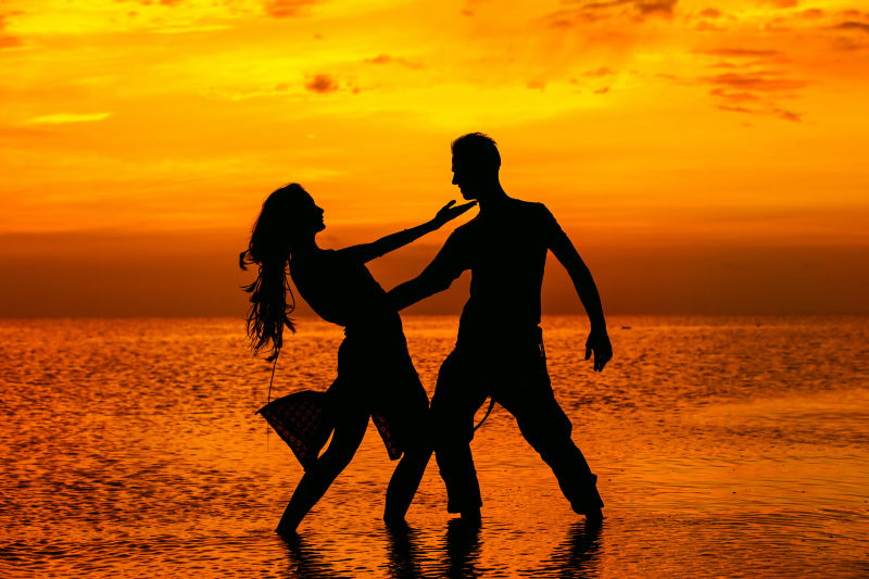 黄昏时在海滩上摆姿势的年轻情侣剪影