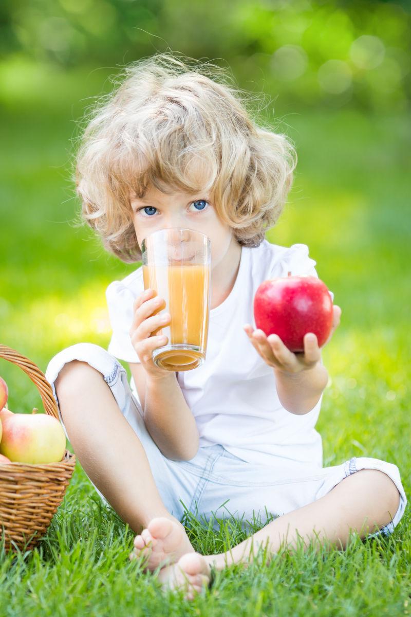 草地上拿着苹果喝着果汁的男孩