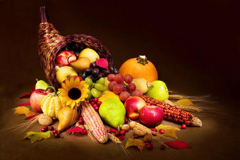 黑色背景下的秋季聚宝盆里的水果蔬菜和花朵
