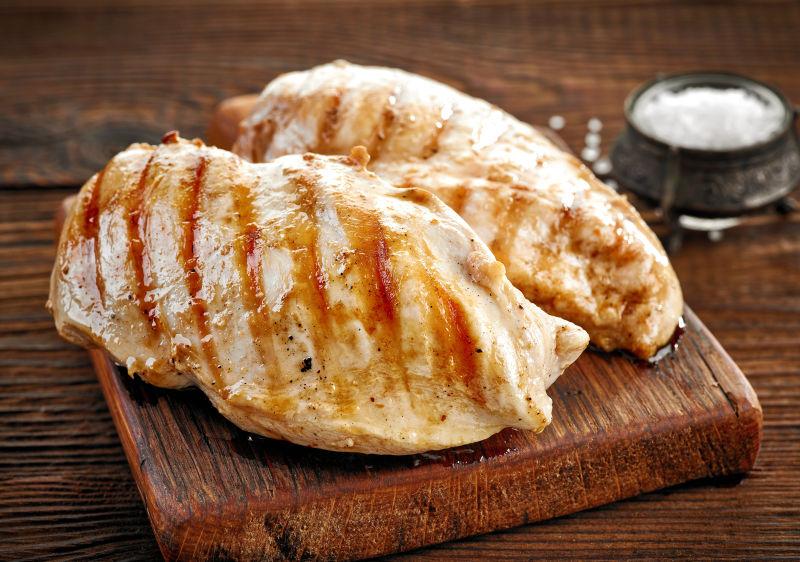 木制菜板上的两块烤鸡胸肉