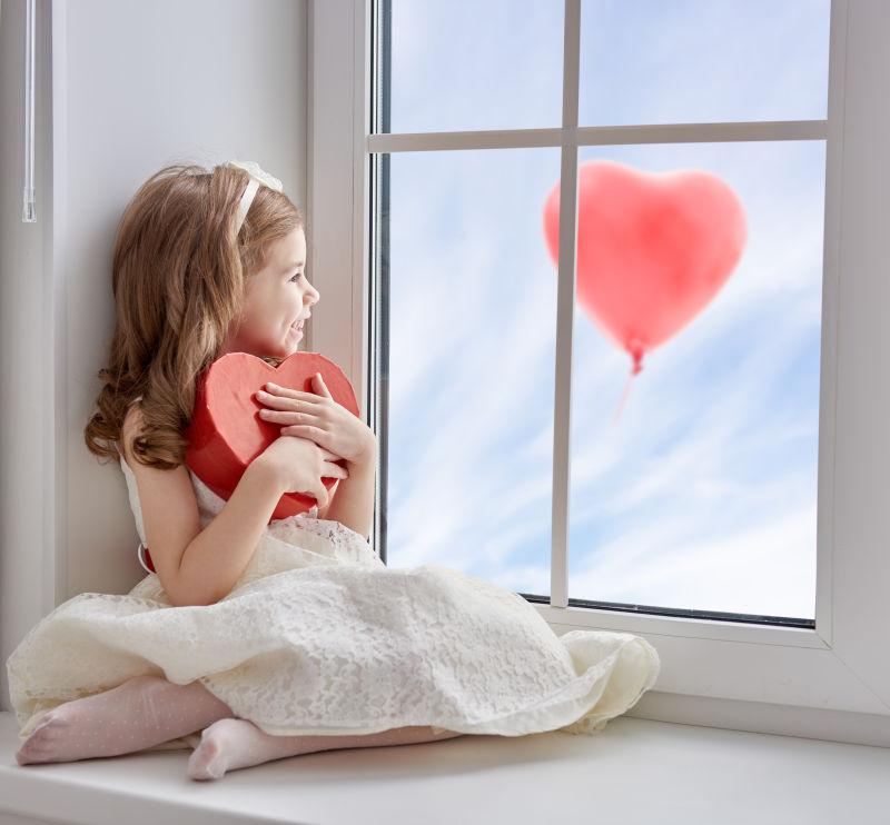 小女孩坐在窗户上拿着红色礼物盒