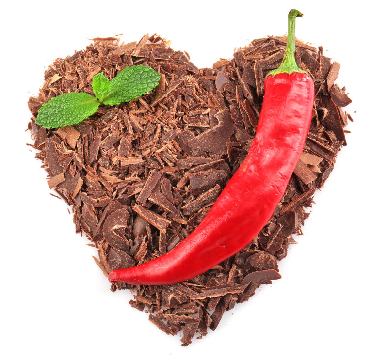 白色背景中的黑巧克力切碎的心脏形状与辣椒