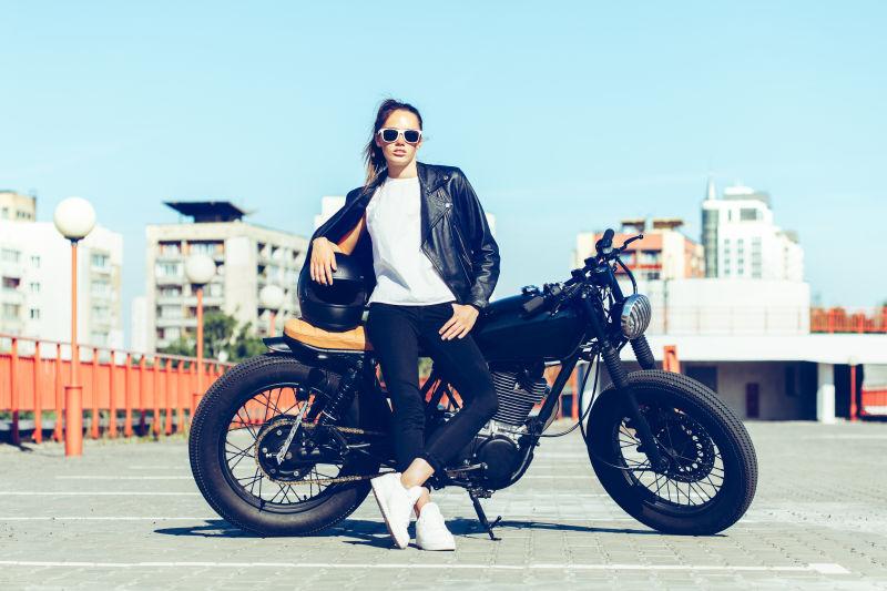 城市建筑背景下穿着黑色皮衣坐在黑色摩托车上的美女