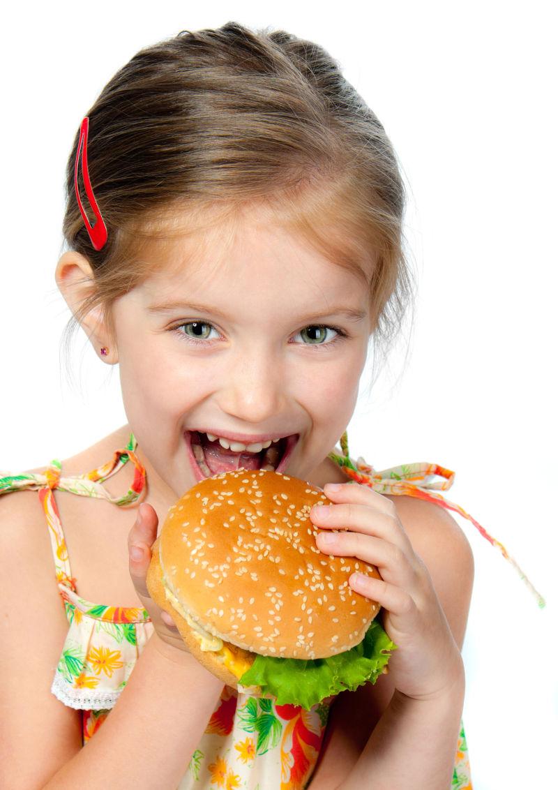 白色背景下吃汉堡的微笑的小女孩