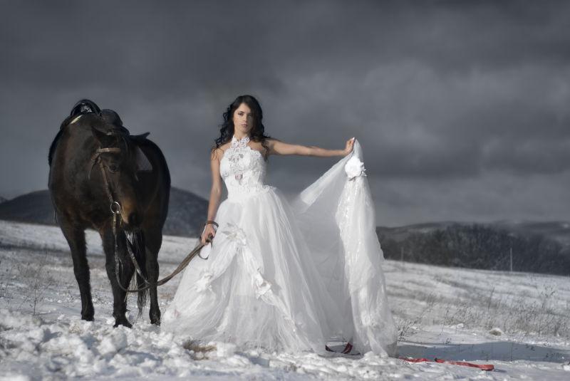 穿白色婚纱牵着马在雪地里的美女