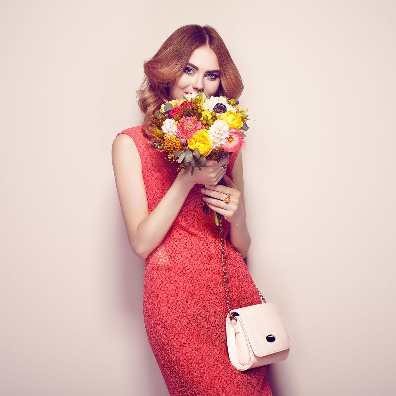 金发碧眼的年轻女人穿着优雅的红色礼服拿着花束