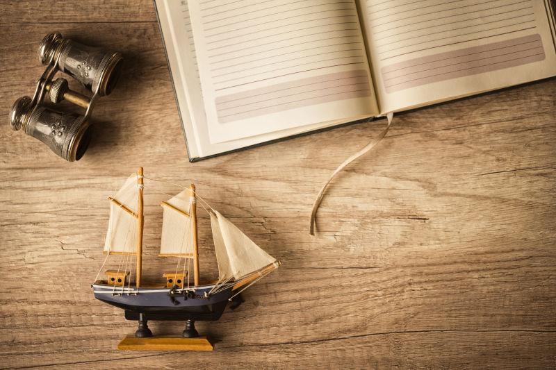 木桌上的帆船模型书本和望远镜等老式旅行用品