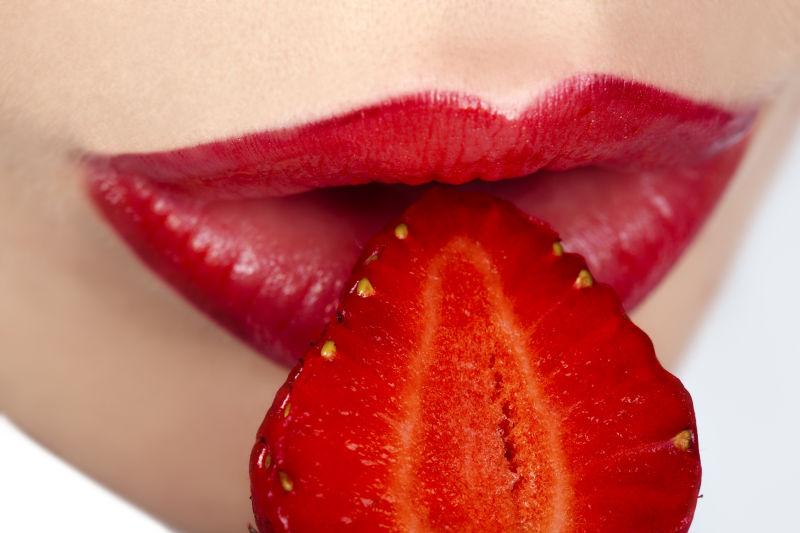 性感的年轻女人嘴里叼着红草莓