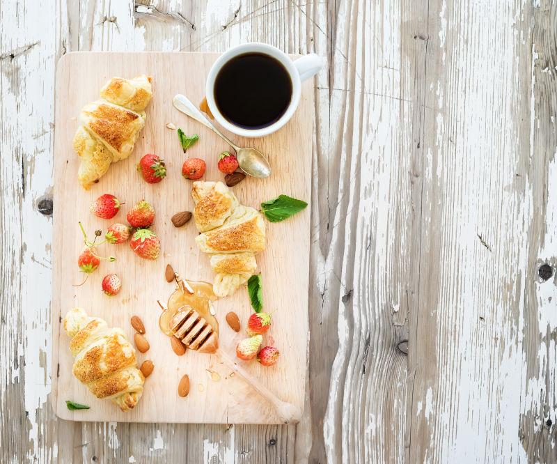 新鲜烤杏仁牛角包配上花园草莓和蜂蜜在白板木底面上