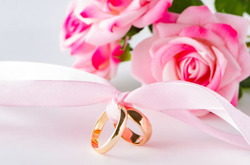 白色桌上粉色玫瑰前使用粉色丝带绑在一起的金戒指