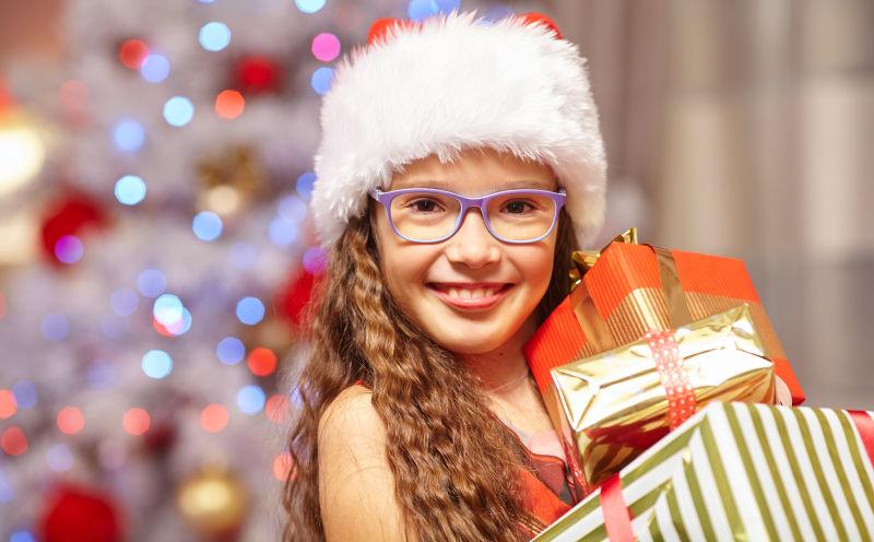在圣诞树前拿着礼物的微笑女孩