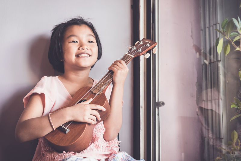 女孩亚洲人出现在音乐学校学习音乐的十年之间弹奏四弦琴教育和音乐的概念