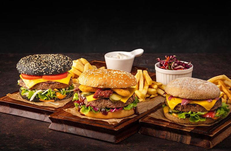 三个自制多汁牛肉芝士汉堡放在木板上-黑底牛肉奶酪汉堡