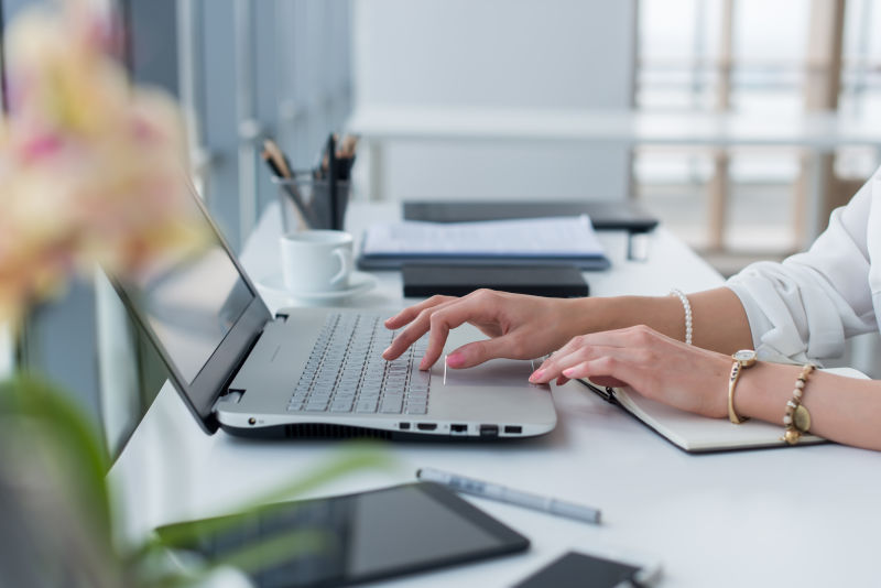 使用键盘在现代办公室的便携式电脑上工作的女性手的特写照片