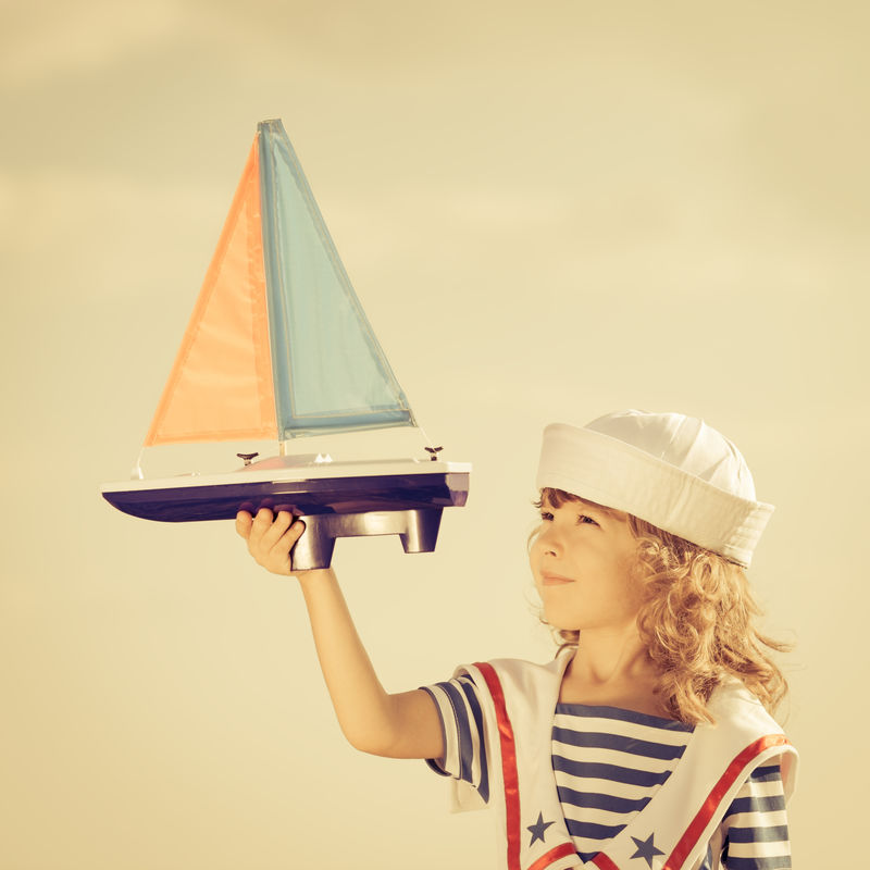 快乐的孩子在夏日天空的背景下玩玩具帆船-旅游度假概念