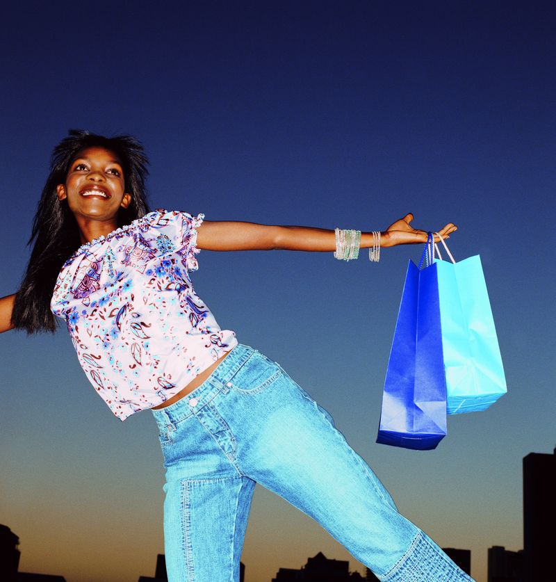 快乐的非洲裔美国妇女拿着五颜六色的购物袋-微笑着-在蓝色的背景下摆姿势-购物狂的内容