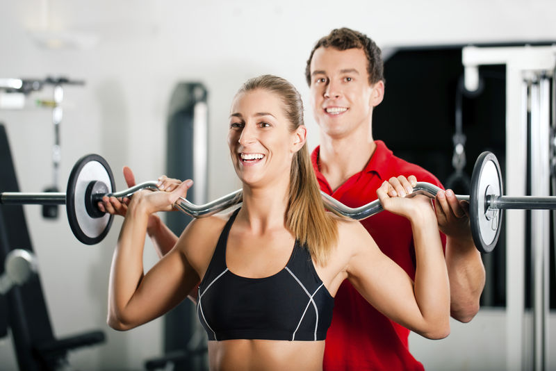 女子在健身房和私人健身教练用杠铃进行力量体操