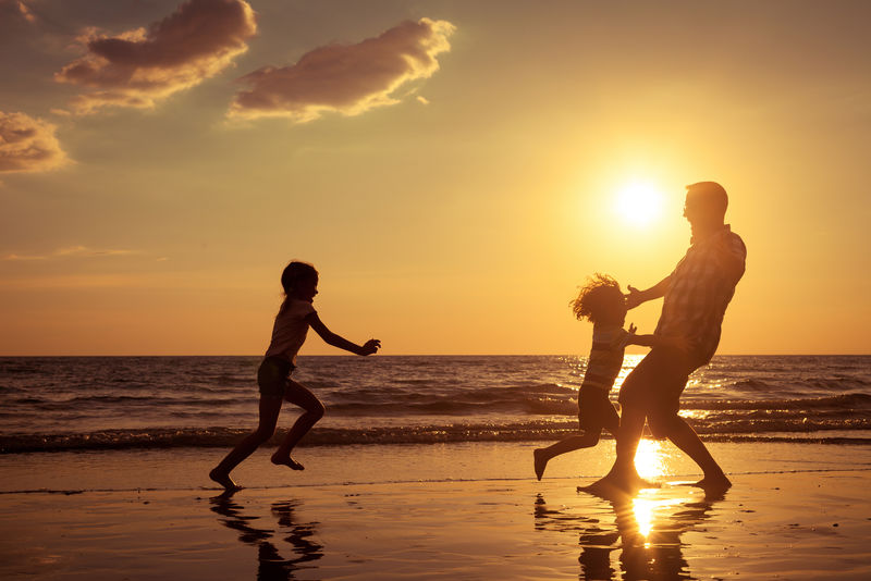 父亲和孩子们在日落时在海滩上玩耍-友好家庭的概念