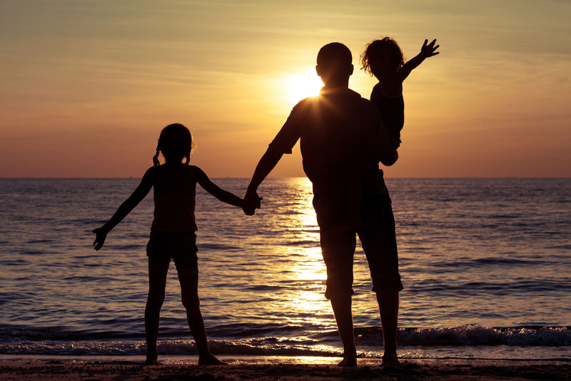 父亲和孩子们在日落时在海滩上玩耍-友好家庭的概念