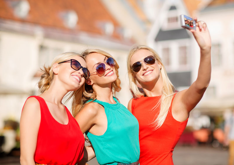 假日旅游和现代科技理念——三个美丽的女孩在城市里用数码相机拍照