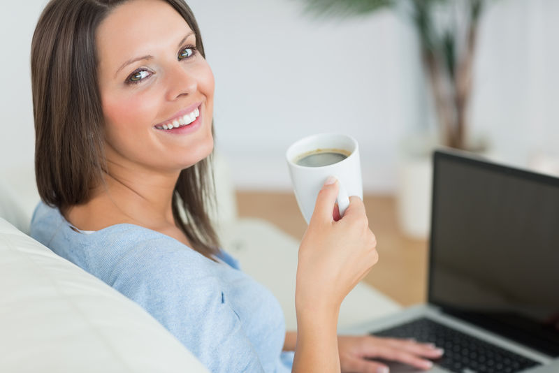 黑发女人用笔记本电脑在客厅里喝咖啡