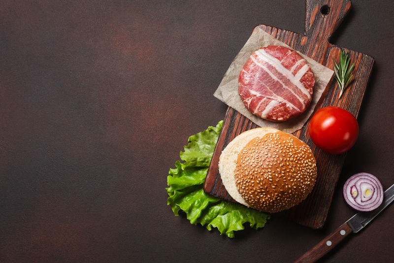 汉堡原料生肉片-番茄-生菜-面包-奶酪-黄瓜和洋葱在生锈的背景上-顶视图和文本放置位置